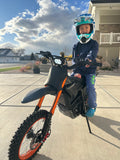 Side view of a blue youth electric dirt bike parked outdoors.